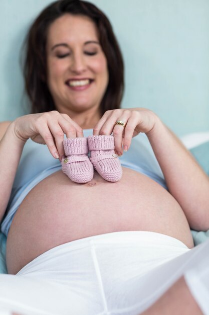 Femme enceinte avec des pantoufles tricotées sur le ventre dans la chambre à coucher