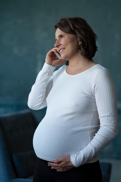 Une femme enceinte parlant au téléphone tient un smartphone, touche son ventre, consulte quelqu'un, future maman exprimant son bonheur.