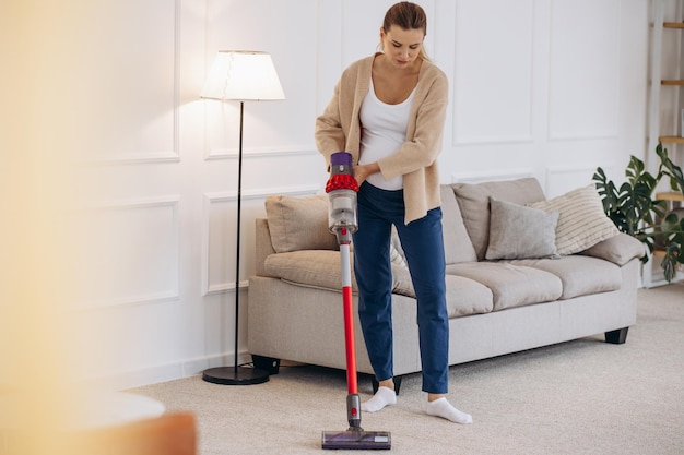 Femme enceinte passant l'aspirateur à la maison avec un aspirateur rechargeable