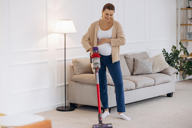 Femme enceinte passant l'aspirateur à la maison avec un aspirateur rechargeable