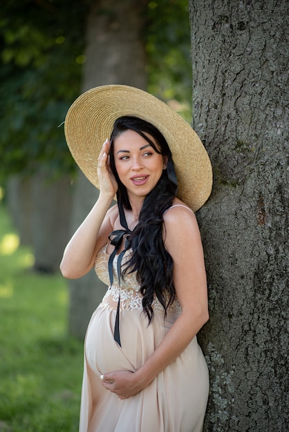 Femme enceinte posant dans une robe beige sur fond d'arbres verts