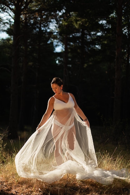 Une femme enceinte pose tenant une partie de sa robe de mariée avec ses mains