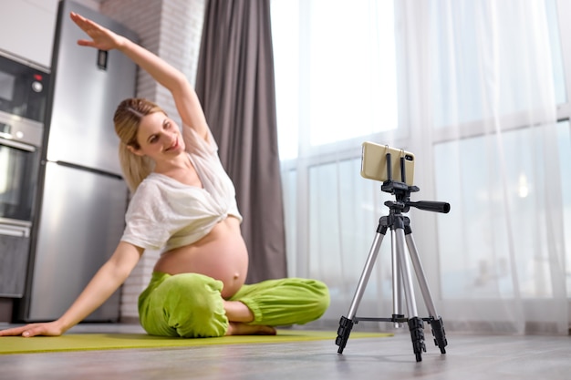 Femme enceinte pratiquant le yoga à la maison avec une future mère de smartphone faisant un cours de formation vidéo prénatale