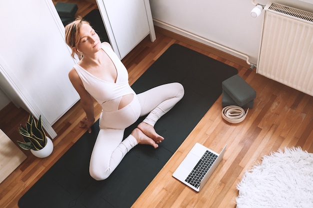 Femme enceinte pratiquant le yoga à la maison avec un ordinateur portable Exercice féminin méditer pendant la grossesse