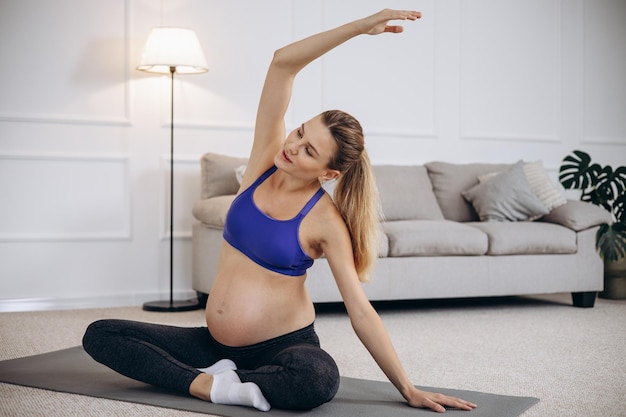 Femme enceinte pratiquant le yoga à la maison sur un tapis