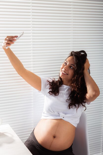 Femme enceinte prenant un autoportrait avec son smartphone pendant le petit déjeuner