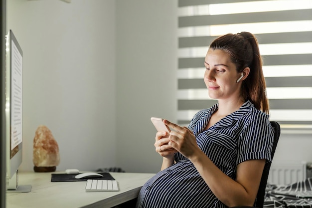 Femme enceinte prenant une pause et utilisant un téléphone au bureau à domicile