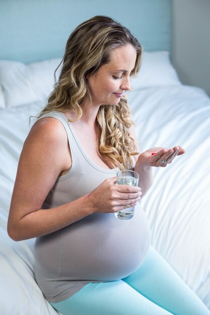 Femme enceinte prenant une pilule avec de l&#39;eau dans sa chambre