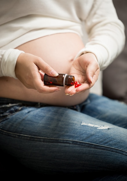 Femme enceinte prenant des vitamines dans des pilules de bouteille en verre