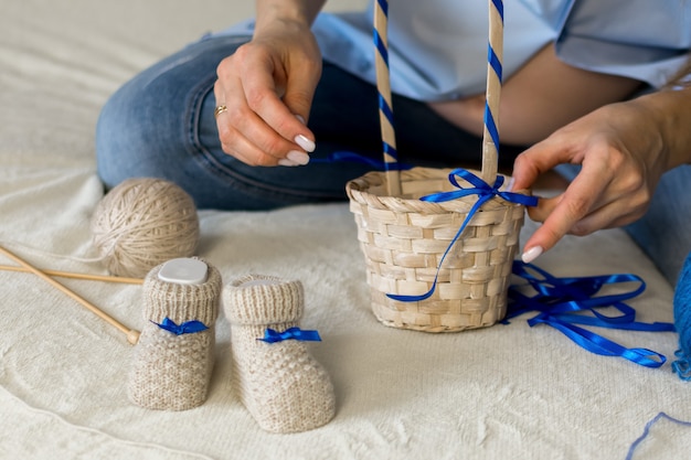 Une femme enceinte prépare un cadeau pour son enfant à naître met des chaussons pour bébé dans un panier en osier