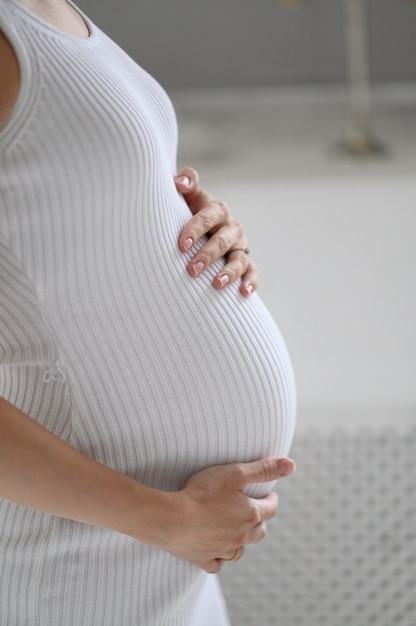 Femme enceinte en pull blanc tenant son ventre