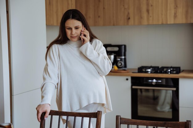 Photo une femme enceinte qui parle au téléphone dans sa cuisine à la maison