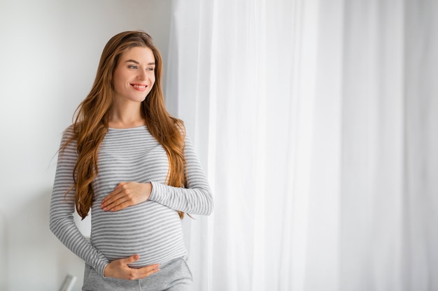 Une femme enceinte qui regarde par la fenêtre.