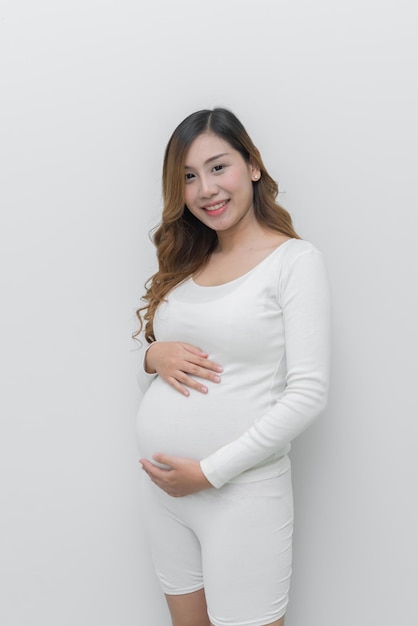 Femme enceinte en robe blanche utilise le toucher de la main sur son ventre sur fond blanc