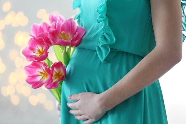 Photo femme enceinte en robe verte tenant des tulipes roses sur fond de paillettes