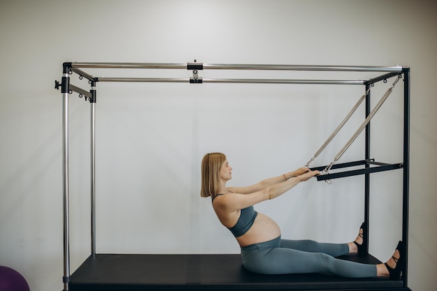 Femme enceinte s'exerçant avec l'aide du réformateur sur la classe de pilates