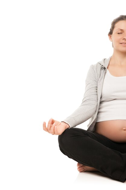 Femme enceinte se détendre en faisant du yoga, assis en position du lotus sur fond blanc