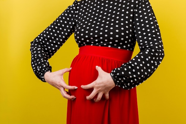 Une femme enceinte se gratte le ventre sur un fond coloré.