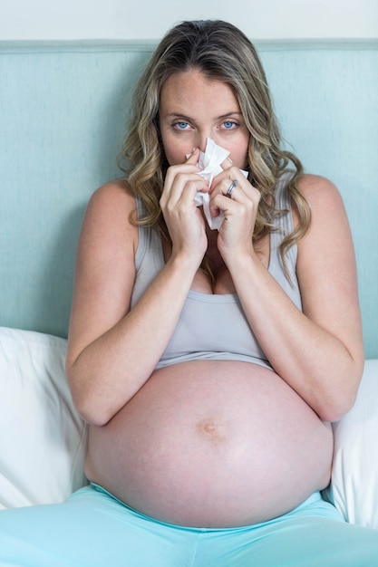 Femme enceinte se mouchant sur son lit