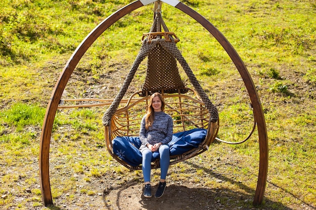 La femme enceinte se repose sur une balançoire avec un oreiller doux sur le fond de la nature