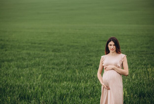 Une femme enceinte se tient sur le terrain avec de l'herbe verte et embrasse son ventre