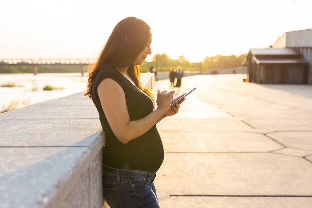 Femme enceinte avec smartphone à l'extérieur de la technologie de la grossesse et du concept de communication