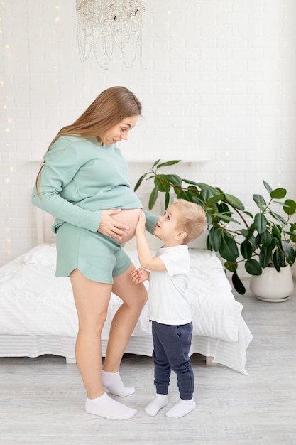 Une femme enceinte et son bébé touchent un gros ventre à la maison sur le lit, le concept de grossesse et attendent la naissance d'un bébé et d'un deuxième enfant dans la famille