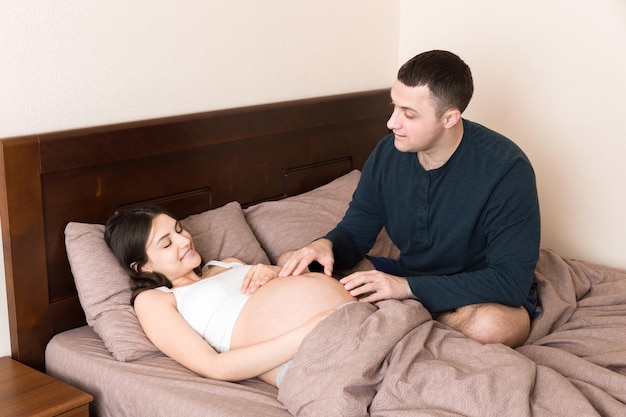 Une femme enceinte avec son mari au lit le matin.