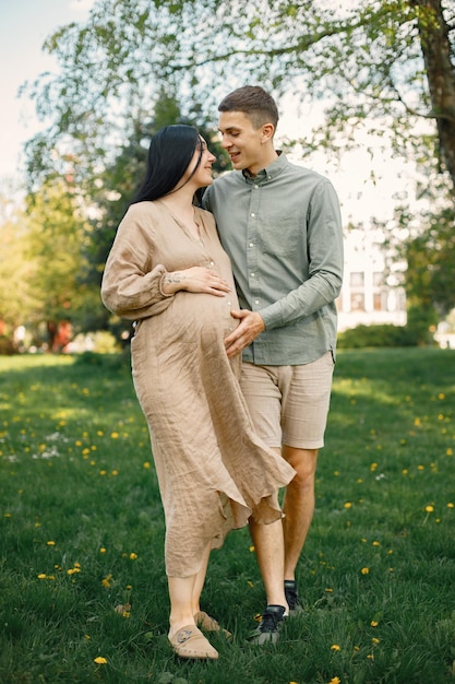 Femme enceinte et son mari debout dans un parc sur une herbe et étreignant