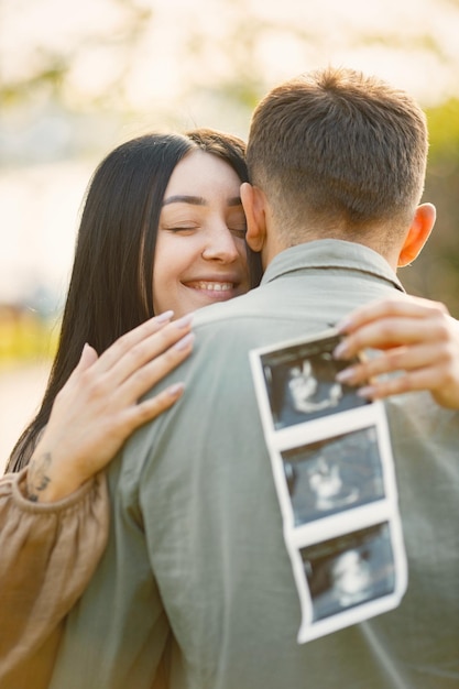 Femme enceinte et son mari debout dans un parc sur une herbe et étreignant