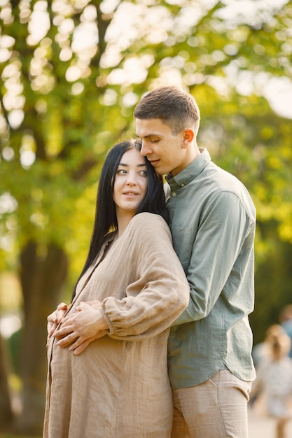 Femme enceinte et son mari debout dans un parc sur une herbe et étreignant