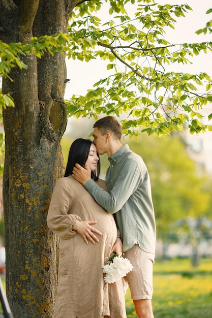 Femme enceinte et son mari debout dans un parc sur une herbe et étreignant