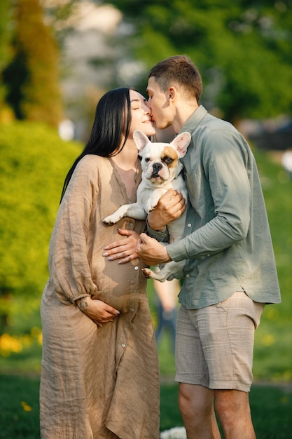 Femme enceinte et son mari debout dans un parc et tenant un petit bouledogue français sur les mains