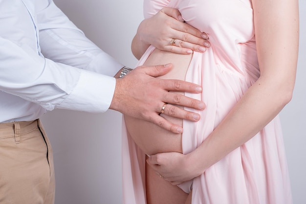 Femme enceinte et son mari sur fond blanc dans le studio gros plan des mains et du ventrexA