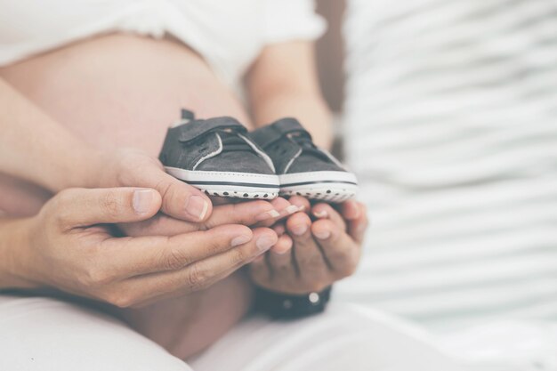 Femme enceinte et son mari main épissure le ventre tenant de petites chaussures pour le bébé à naître