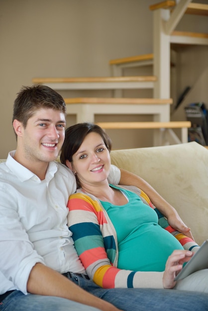 une femme enceinte avec son mari s'amuse à se détendre et à utiliser une tablette à la maison moderne