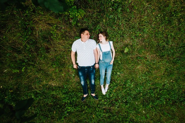 Une femme enceinte et son mari sont heureux de s'allonger sur l'herbe à l'extérieur. Vue de dessus.