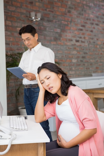 Femme enceinte souffrant assis à la maison pendant que son mari utilise une tablette