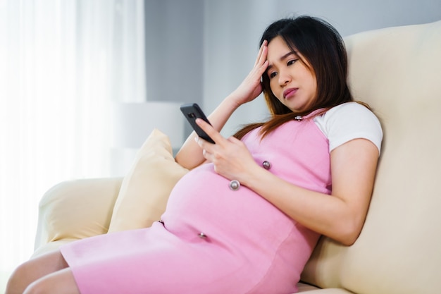 Femme enceinte a souligné à l'aide d'un smartphone sur un canapé dans le salon