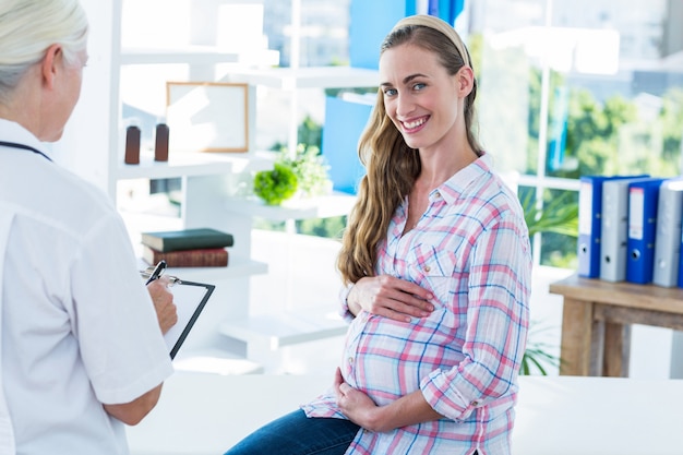 Femme enceinte, souriant à la caméra sur une table d&#39;examen