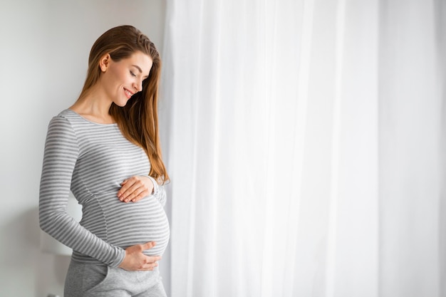 Une femme enceinte souriant avec les yeux fermés.