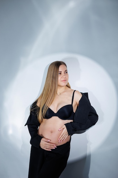 Femme enceinte souriante dans un costume noir sur fond gris Belle femme enceinte élégante