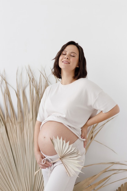 Femme enceinte souriante dans un style bohème. Une jeune fille enceinte dans un style écologique, sur un fond blanc vide.