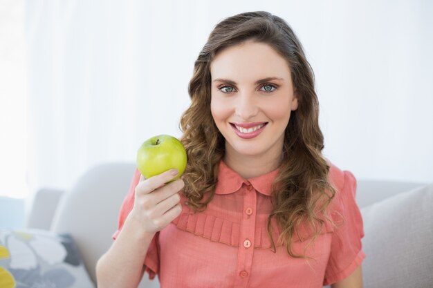 Femme enceinte souriante présentant une pomme verte assis dans le salon