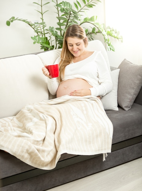 Femme enceinte souriante se détendre sur un canapé avec une tasse de thé