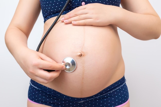 la femme enceinte utilise un stéthoscope pour écouter le cœur du bébé.  écouter les voix de l'enfant à naître crée une relation entre la mère et  l'enfant à naître. concept bonheur de