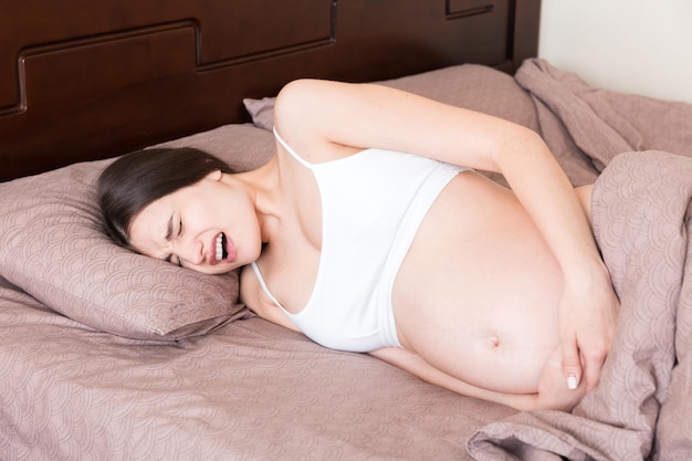 Femme enceinte stressée allongée dans son lit avec sa main sur son ventre grimaçant du boulon