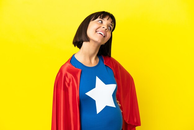 Femme enceinte de super héros isolée sur fond jaune pensant à une idée tout en levant les yeux