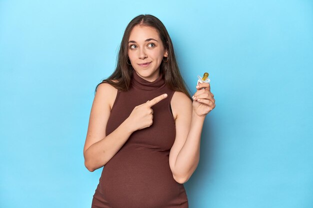 Femme enceinte tenant un anneau de dentition pour bébé dans un studio bleu