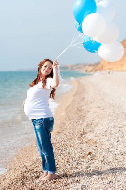 Femme enceinte tenant des ballons à air à l'extérieur. Marcher au bord de la mer. Maternité.